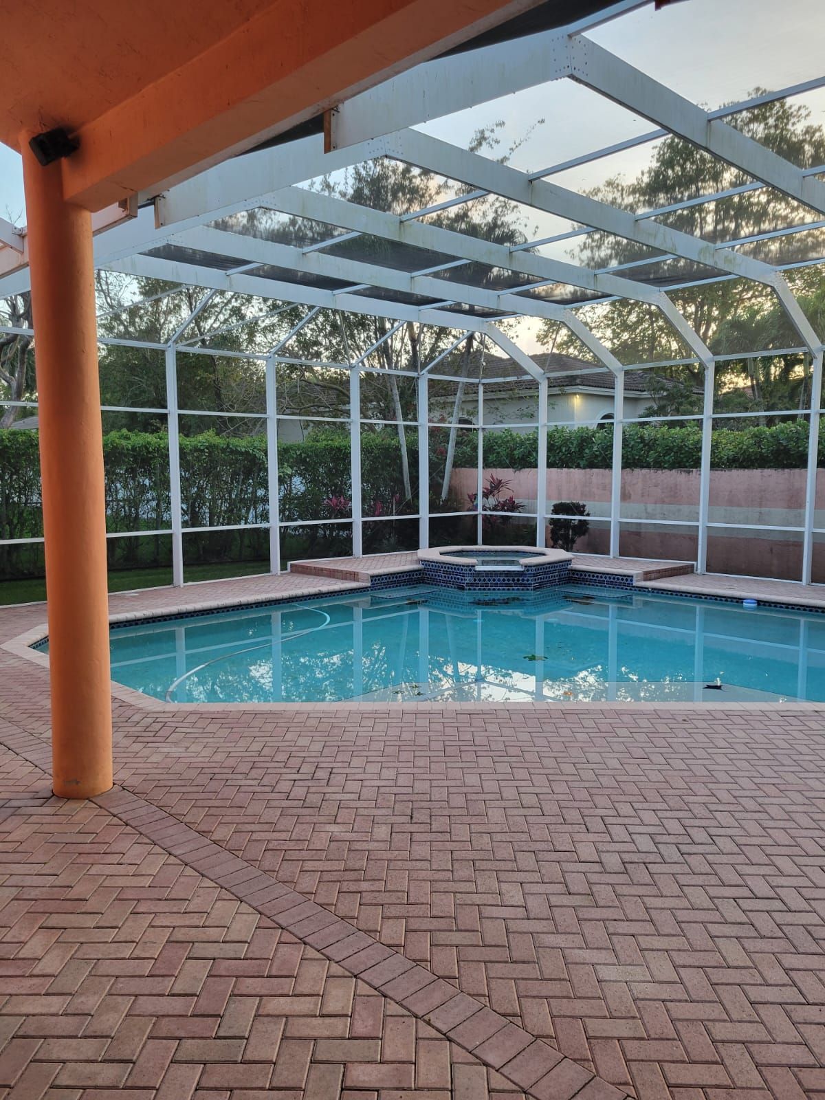 Covered backyard pool with brick patio and screened enclosure under a white roof