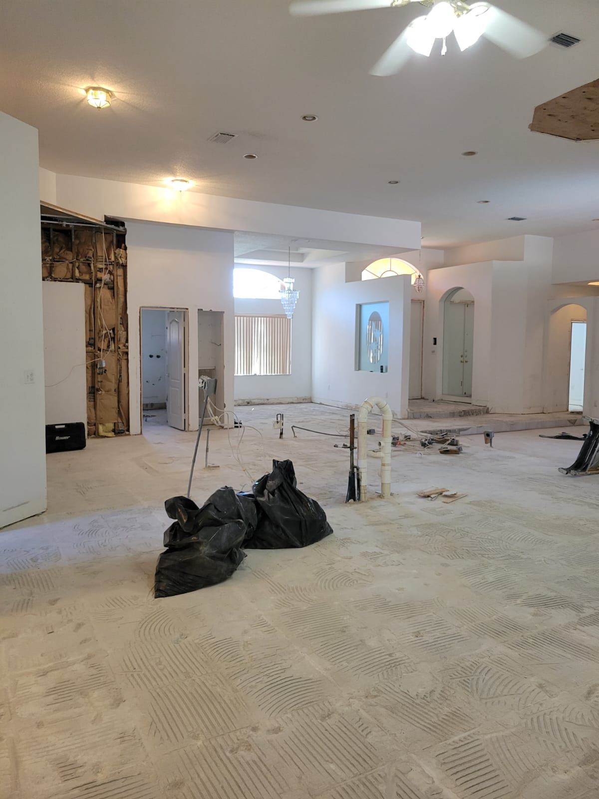 Renovation in progress in a large white room with debris, tools, and exposed wall framing on the floor.