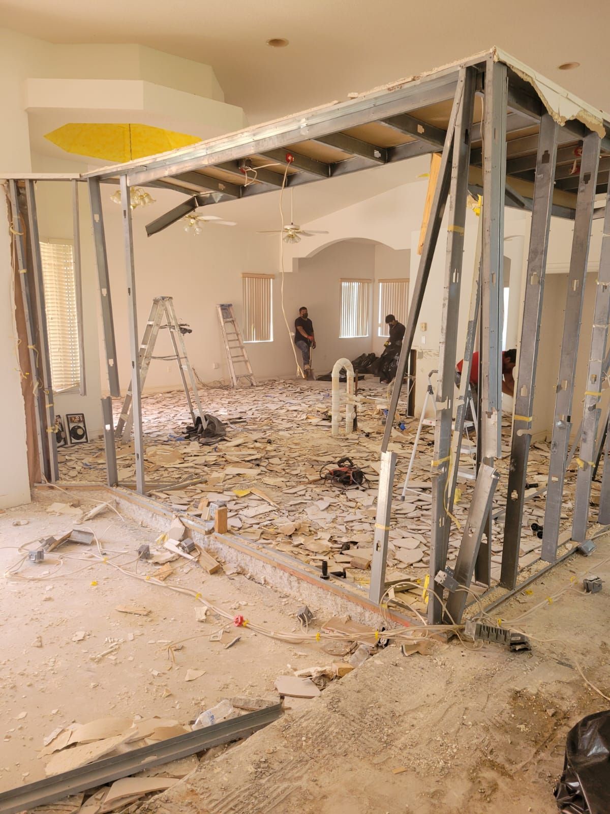 Interior under construction with exposed framing, debris-covered floor, and ladders in a partially demolished room