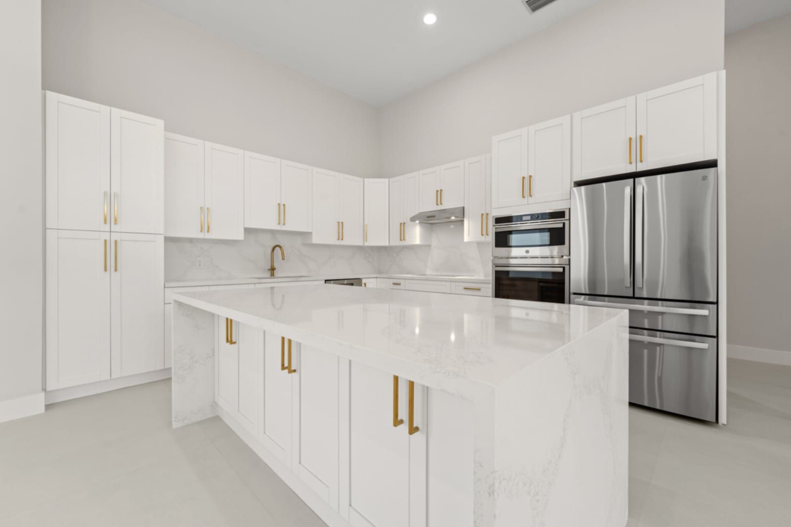 Bright white modern kitchen with marble island, gold handles, and stainless steel appliances