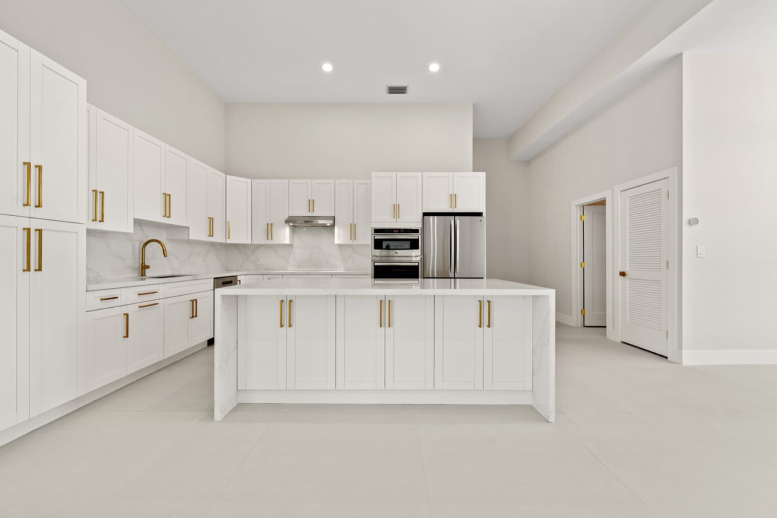 Bright white modern kitchen with gold hardware, center island, and built-in stainless steel appliances