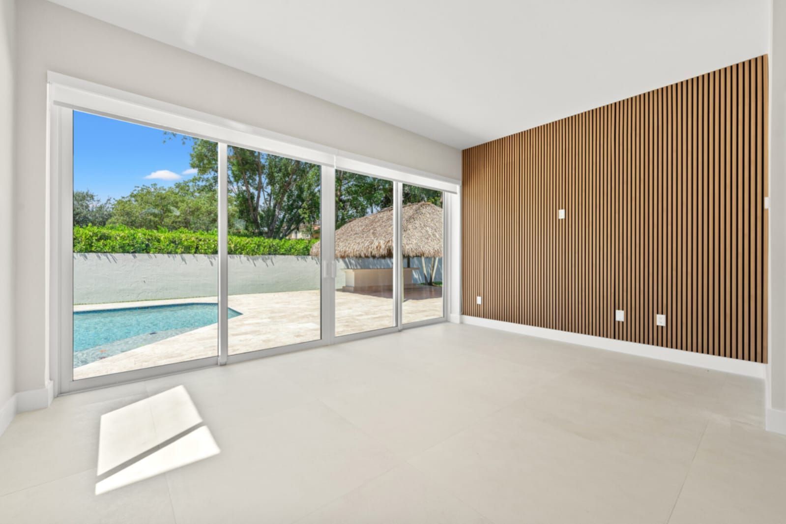 Bright empty room with sliding glass doors, pool view, and a wooden accent wall