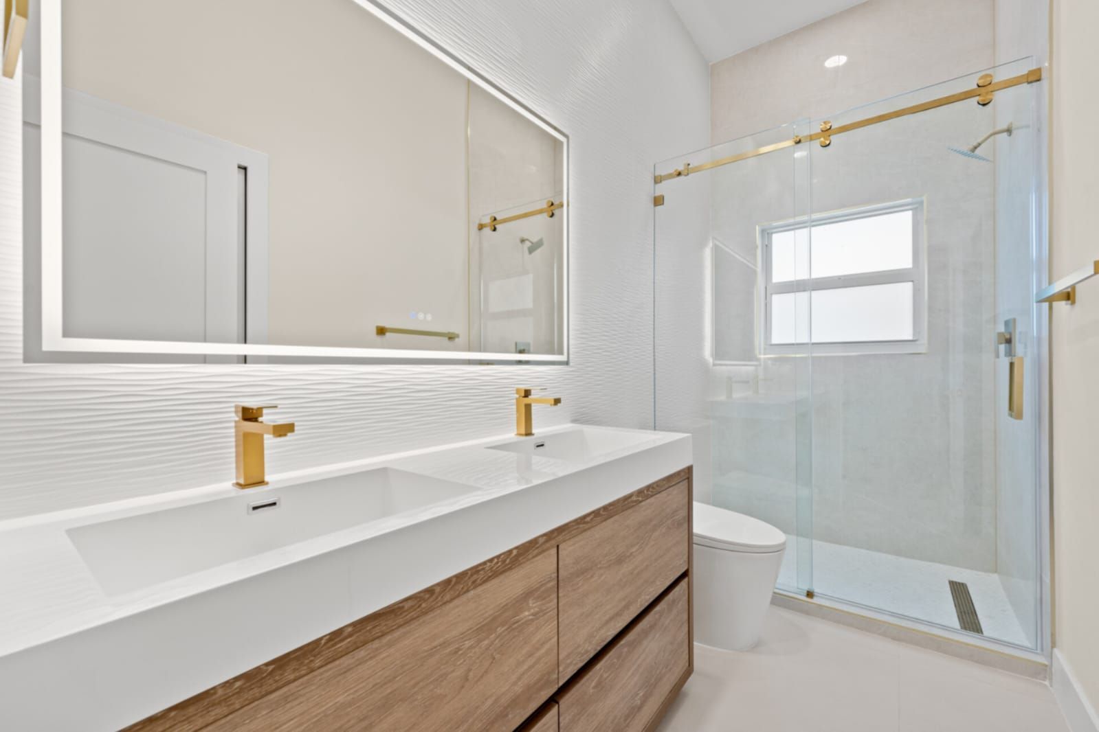 Modern bathroom with double vanity, gold fixtures, and glass shower enclosure
