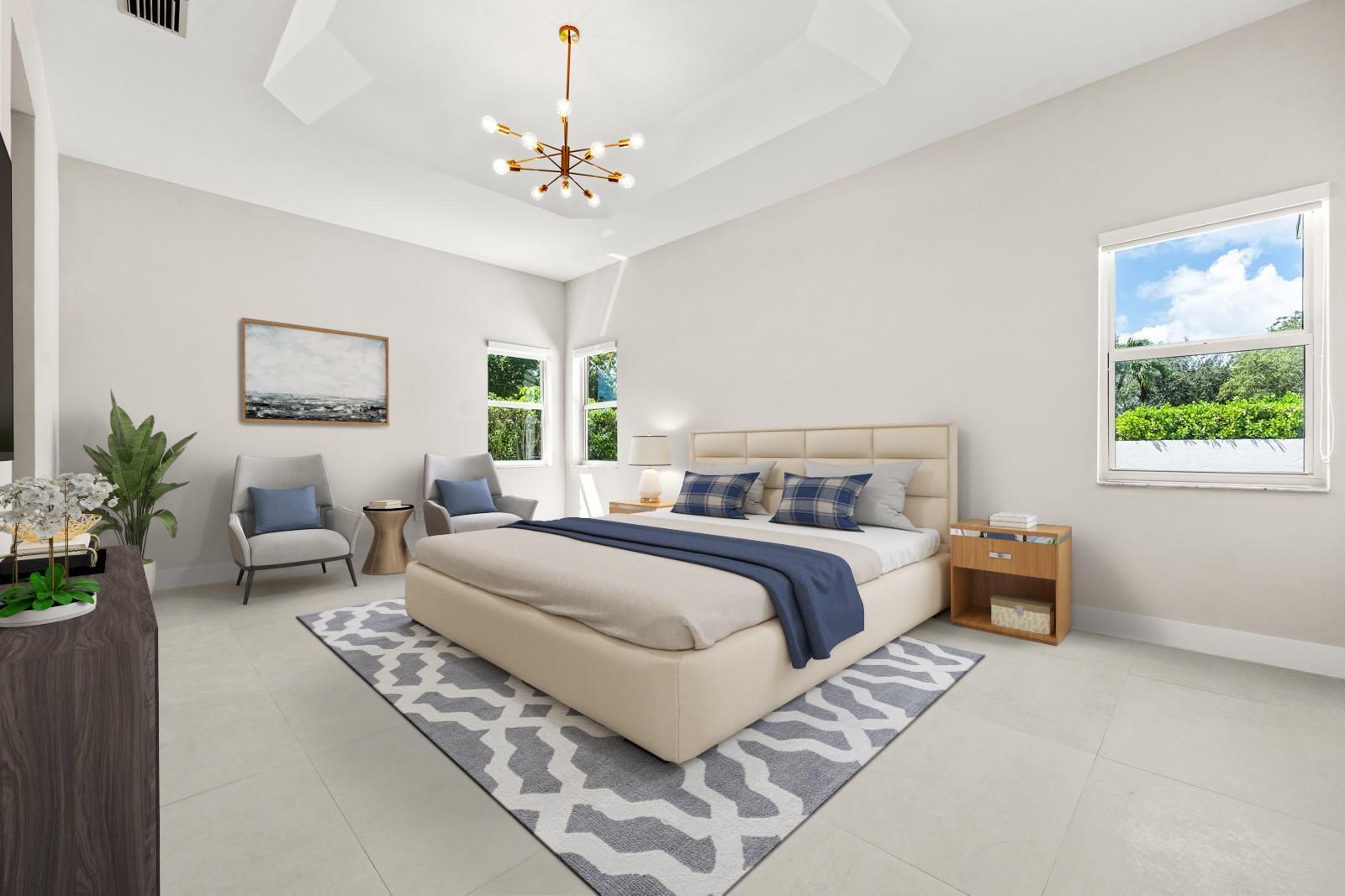 Bright modern bedroom with a beige bed, gray rug, chair, nightstand, and large windows.
