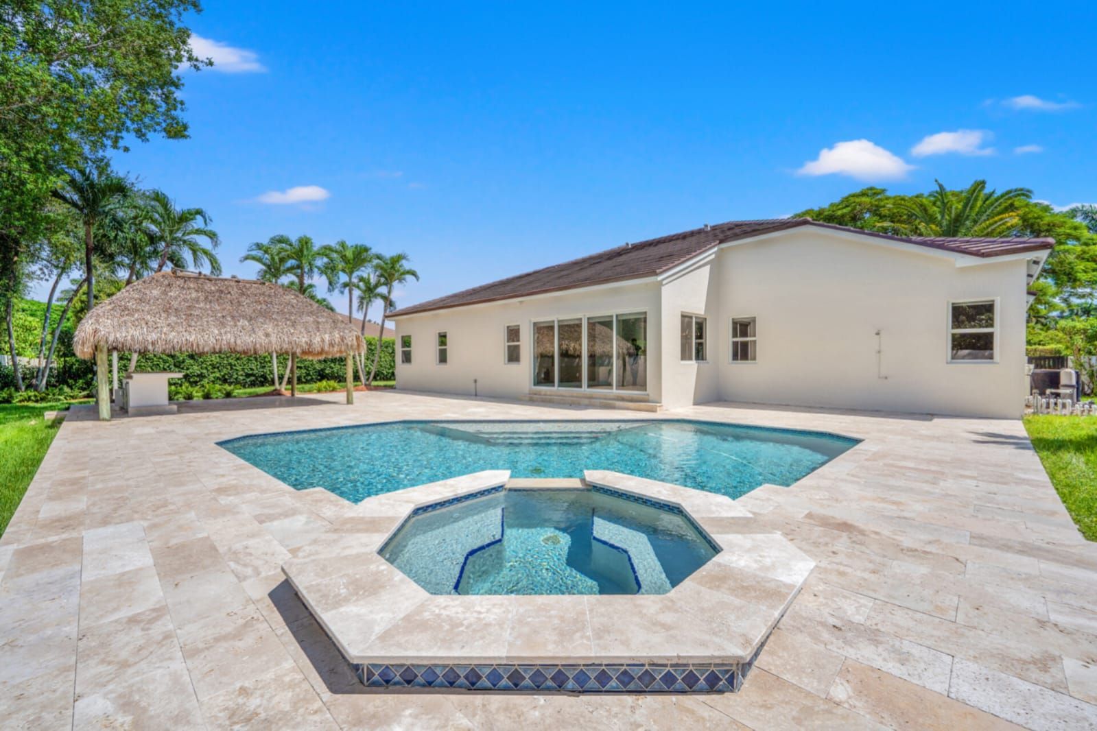 Modern backyard with turquoise pool, hot tub, paved patio, and a thatched gazebo beside a white house