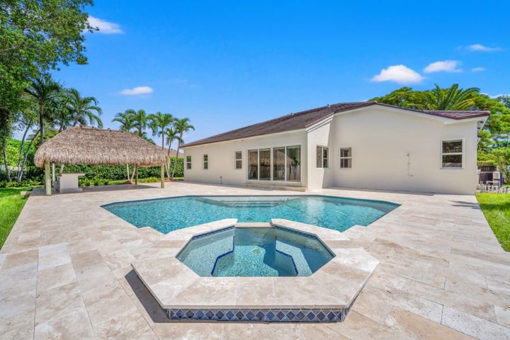 Backyard patio with a swimming pool, spa, and thatched cabana beside a modern house
