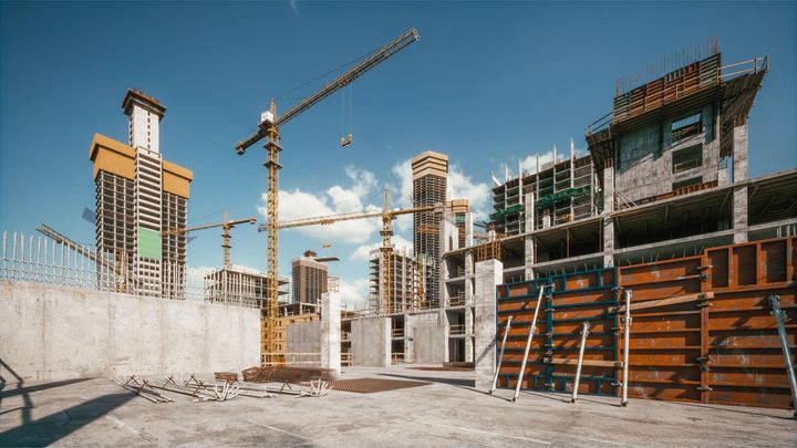 Construction site with cranes, unfinished concrete buildings, and scaffolding under a clear blue sky