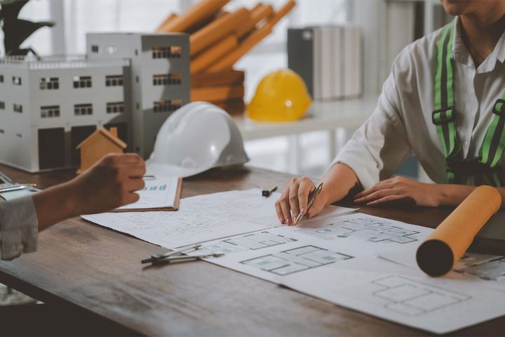 Architects reviewing blueprints at a construction site table with hard hats and rolled plans