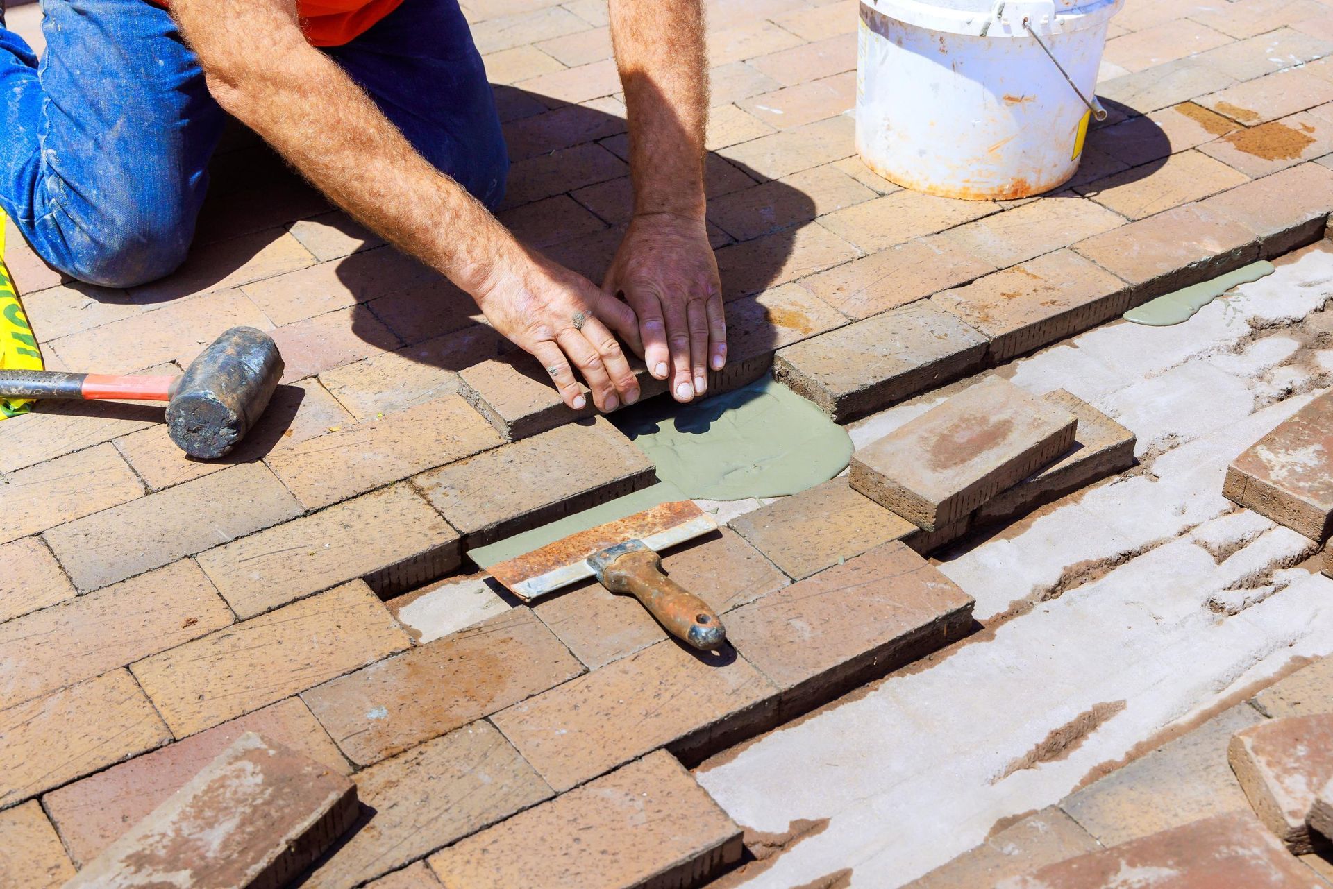 Worker installing paving stones with a mallet and trowel on a brick walkway