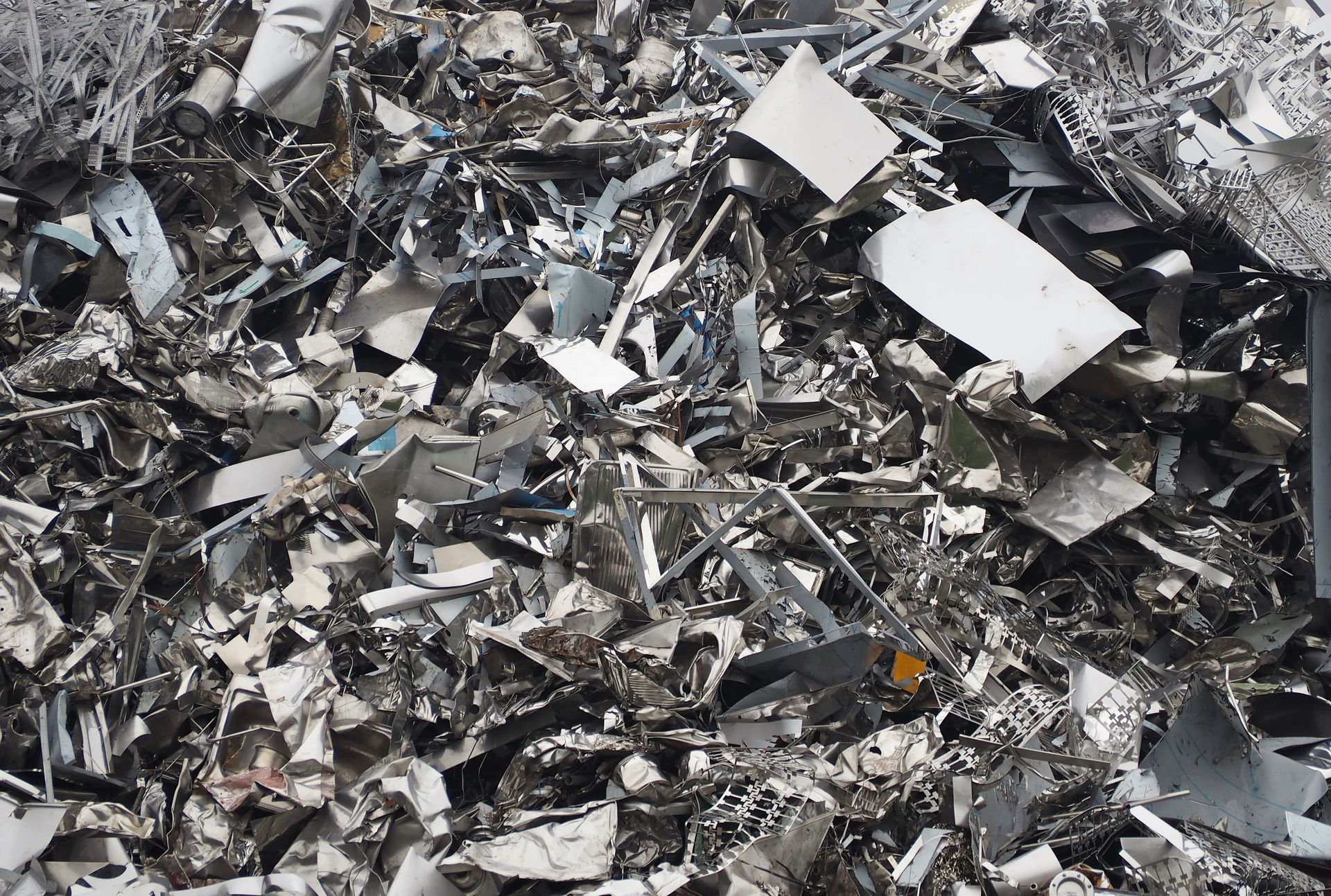 Large pile of mixed scrap metal sheets and fragments, showing industrial recycling materials.