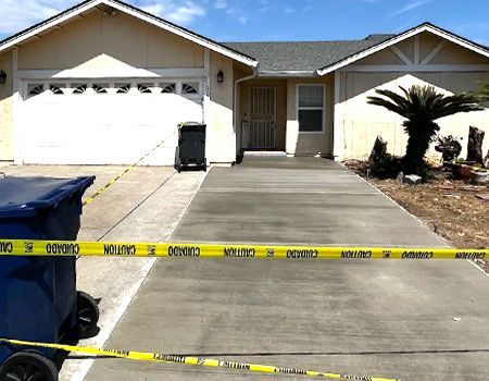 A blue trash can sits in front of a house with yellow tape that says caution