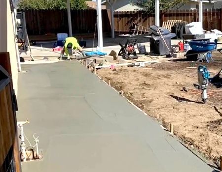 A man is working on a concrete walkway in a backyard.