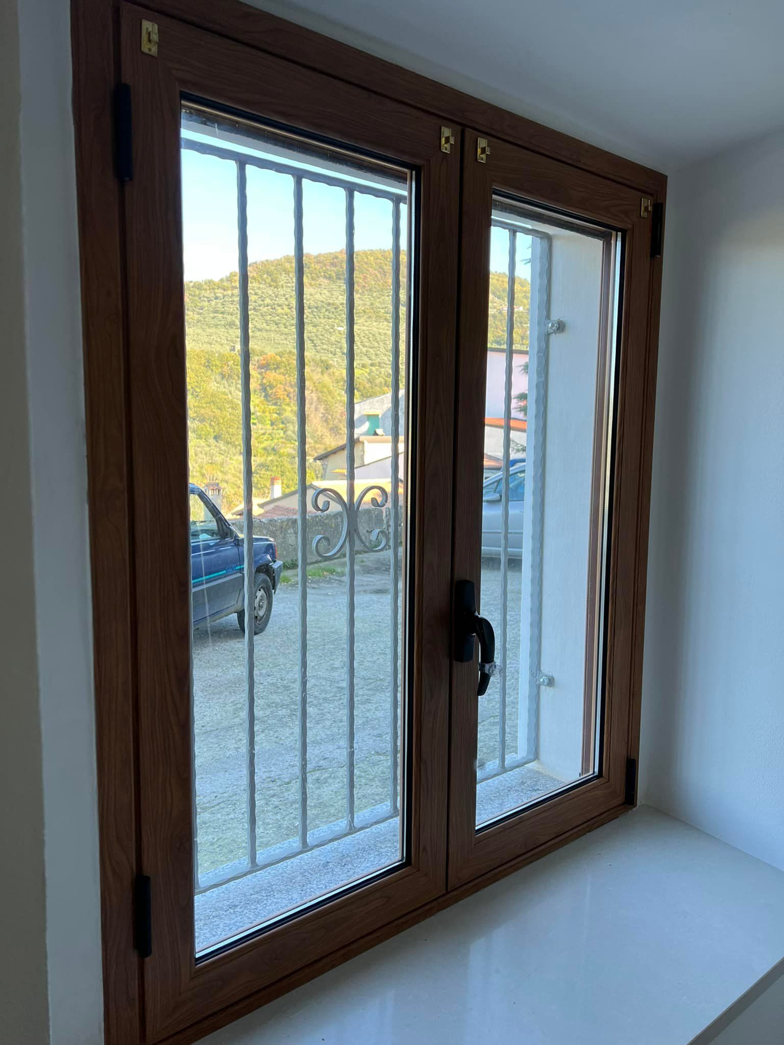 Finestra con telaio in legno e inferriate di sicurezza. Vista sulla strada e sulle colline circostanti.