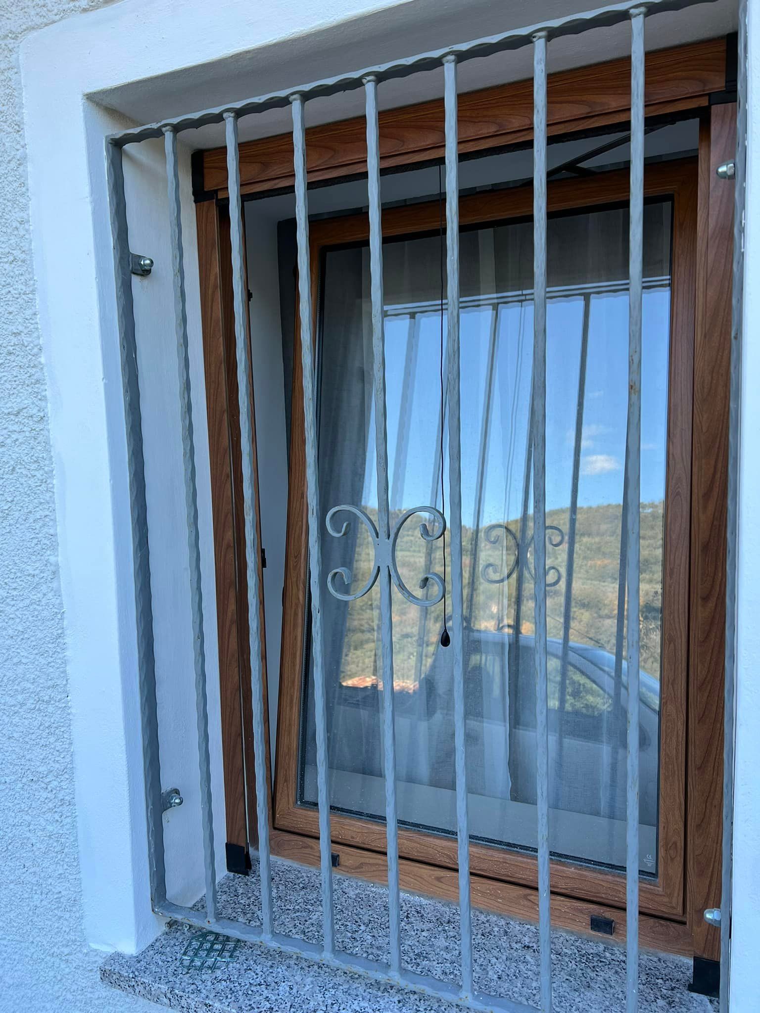 Finestra con sbarre di sicurezza e telaio in legno su una parete in stucco bianco.