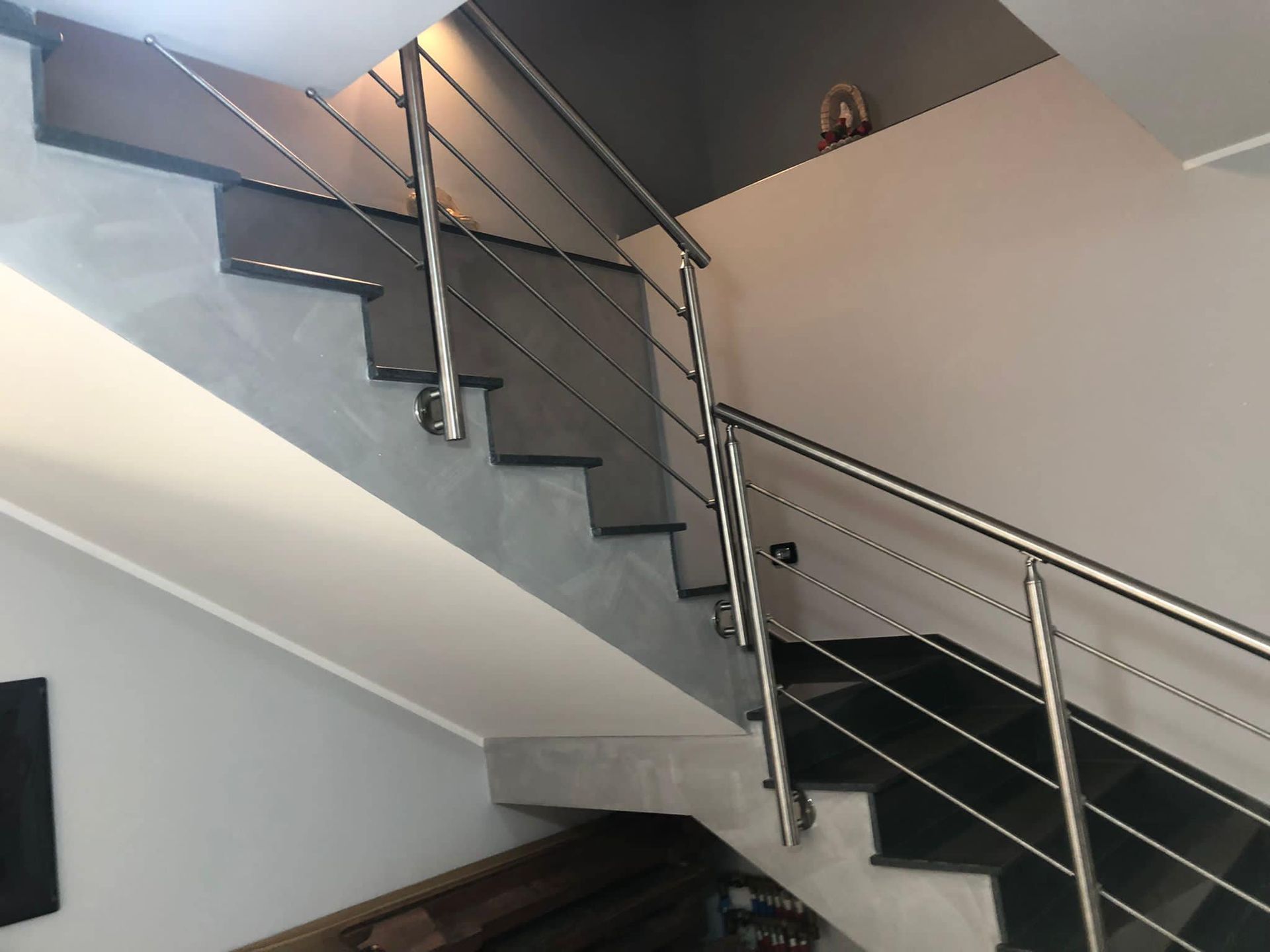 Scala con ringhiera in acciaio inox e gradini scuri. Le pareti sono grigie e bianche.