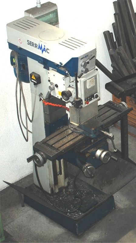 In un'officina, su un pavimento scuro, si trova una fresatrice industriale Serrmac di colore bianco e blu.
