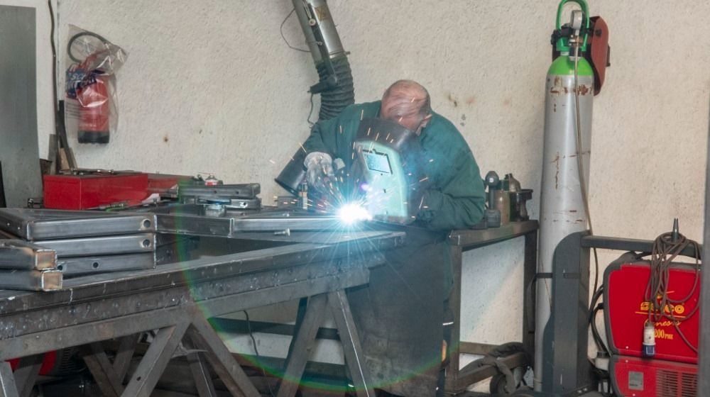 Un saldatore lavora a un banco da lavoro in un'officina, le scintille volano mentre salda pezzi di metallo.