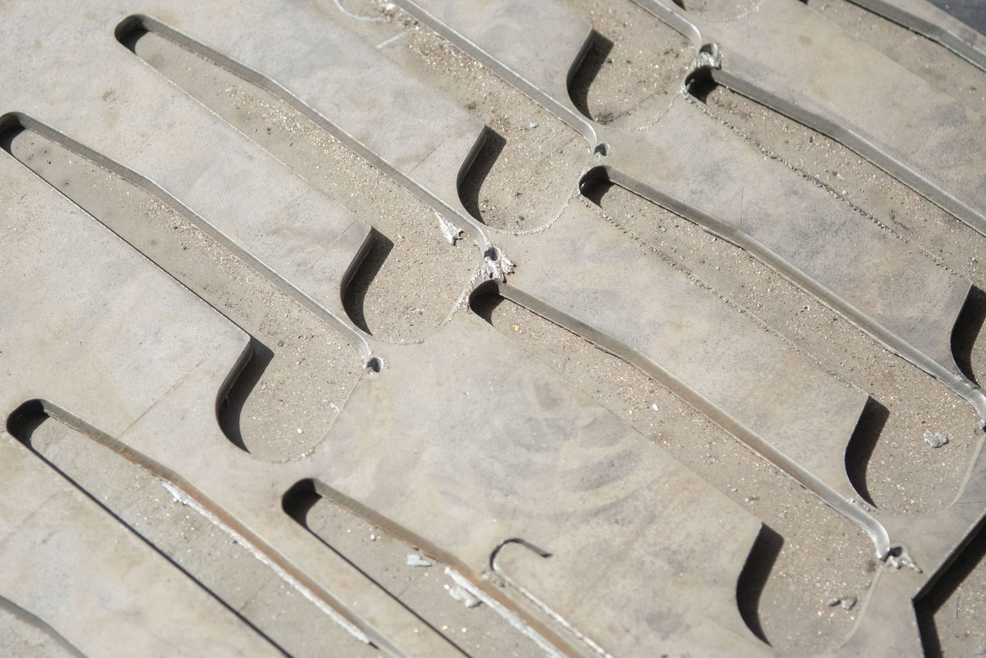 Primo piano di una griglia di scarico in metallo grigio con aperture a fessura ripetute e una superficie ruvida simile al cemento.
