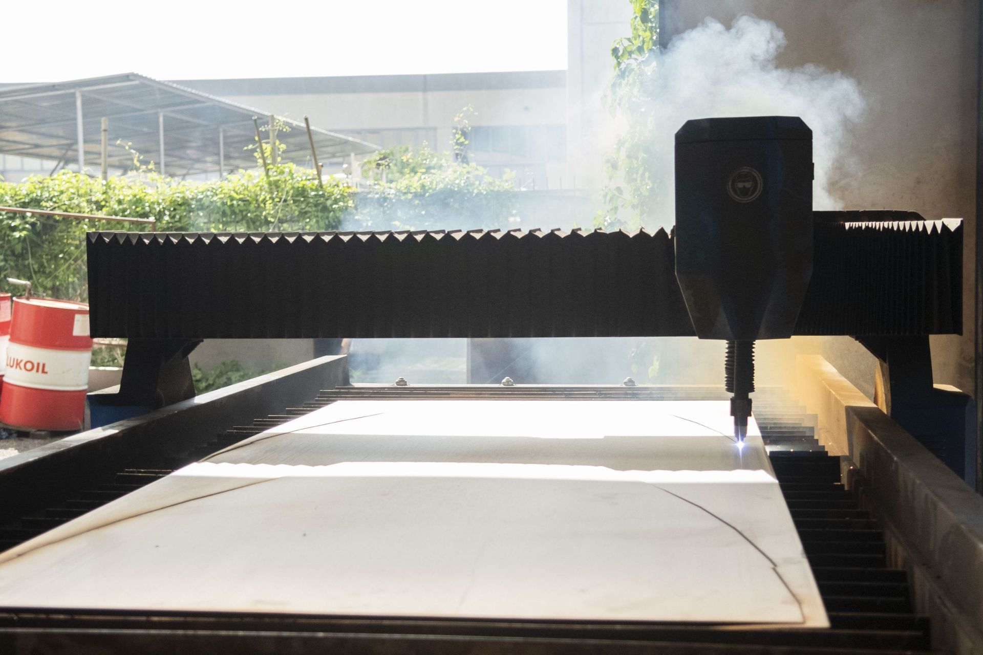 In un'officina, una macchina da taglio laser a controllo numerico (CNC) sta attivamente tagliando una forma su un grande foglio di materiale, emettendo fumo.
