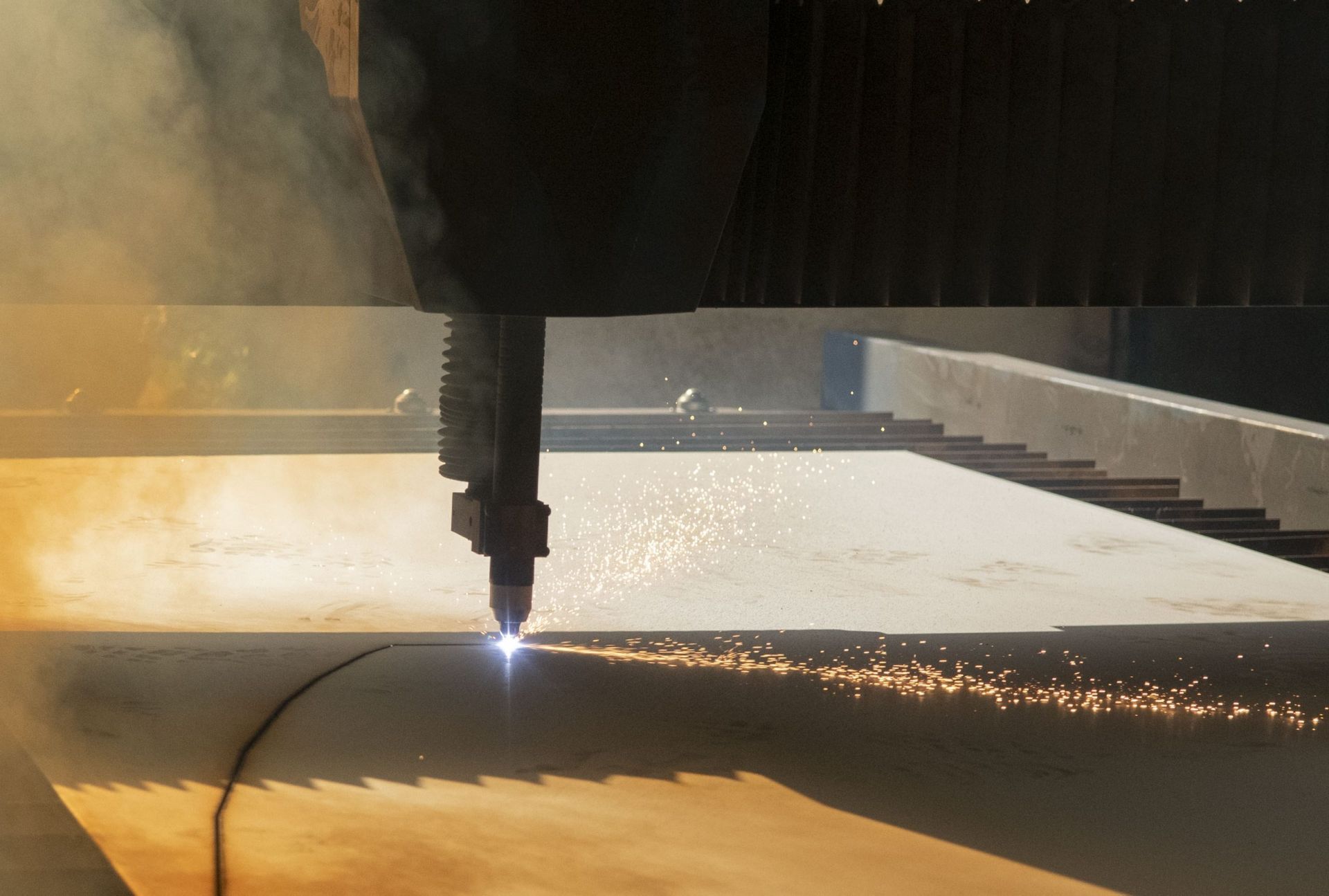 Un utensile da taglio laser che trancia una lamiera metallica, creando scintille luminose in un ambiente industriale.