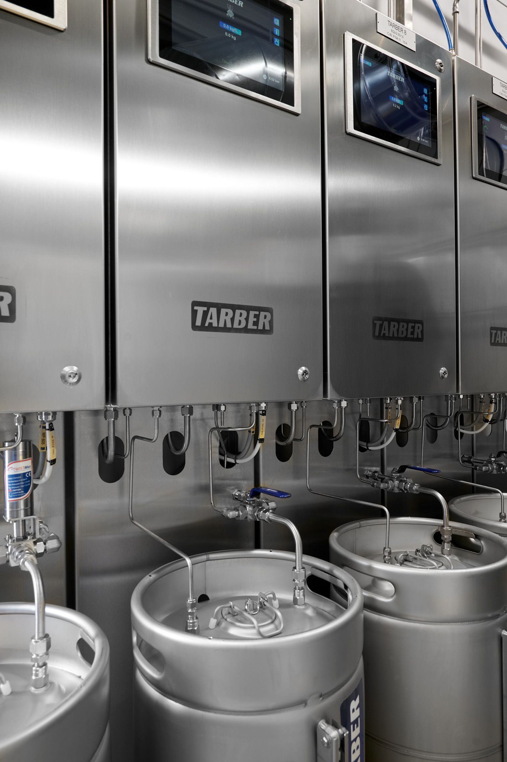 A row of stainless steel kegs are lined up next to each other.