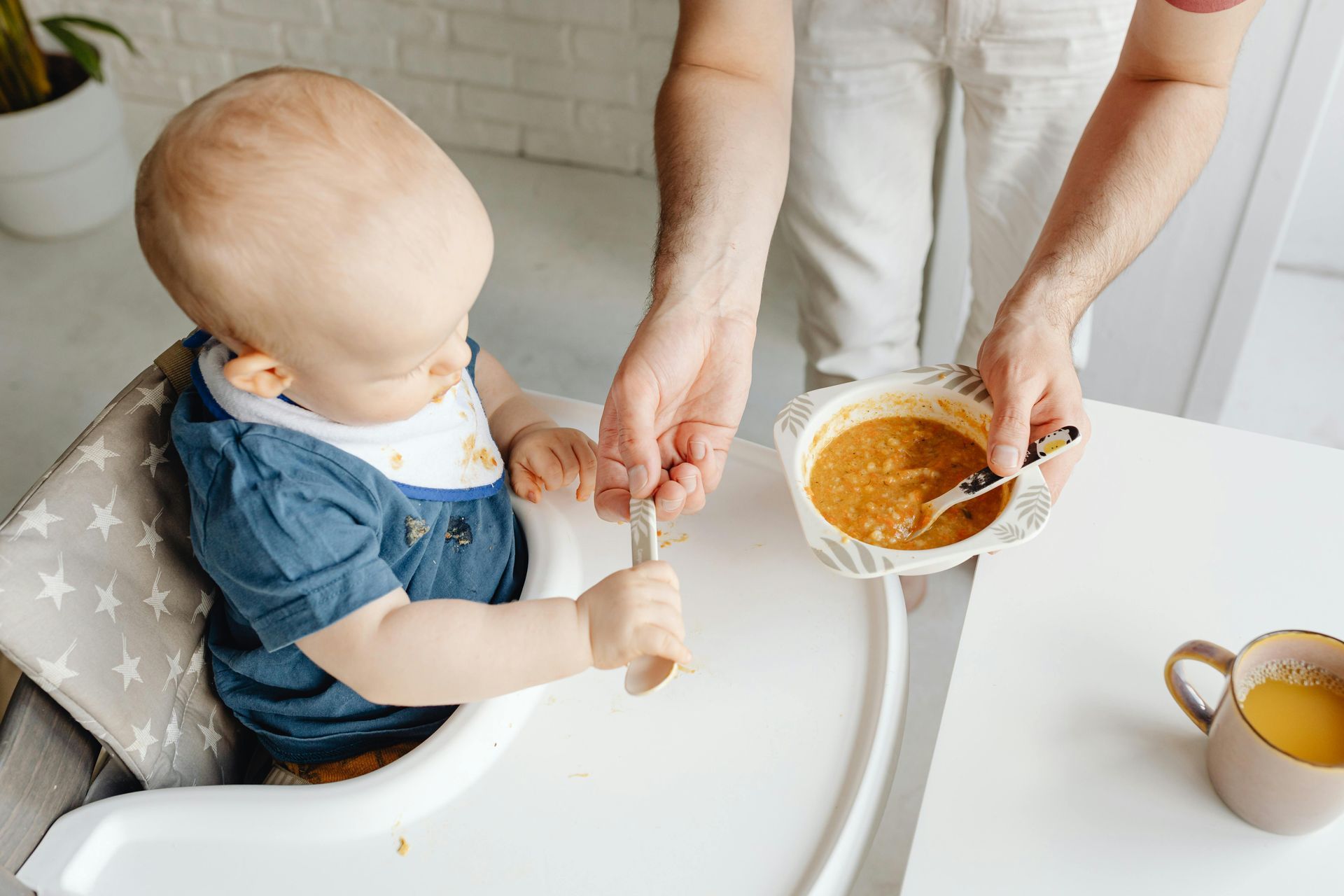 A woman is feeding a baby in a high chair with a spoon.