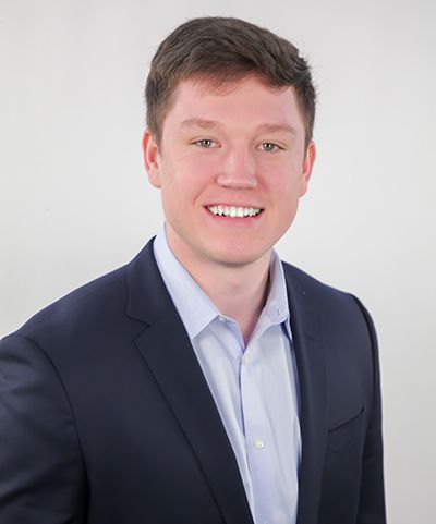 A young man in a suit and white shirt is smiling for the camera.