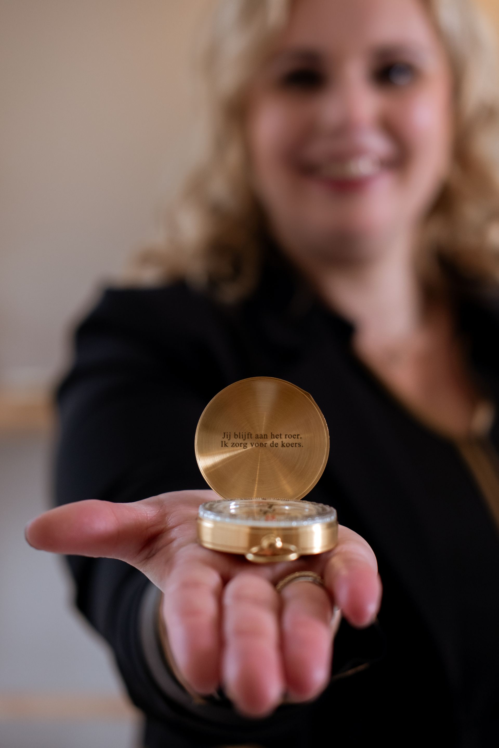 Een vrouw houdt een ronde, gouden doos open en glimlacht. Op de doos staat een inscriptie.