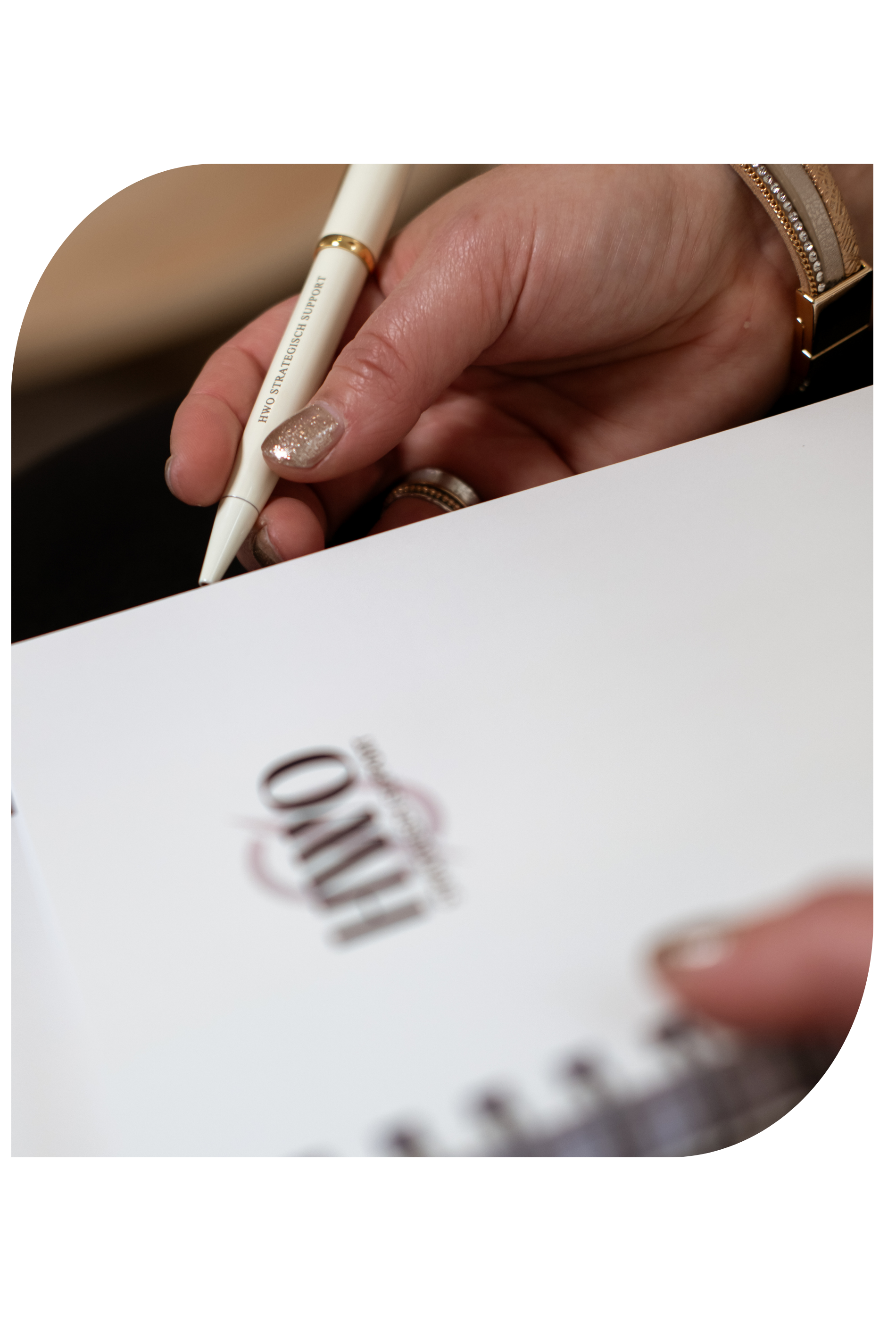 De hand van een persoon met gouden nagellak, die schrijft in een notitieboekje met het woord