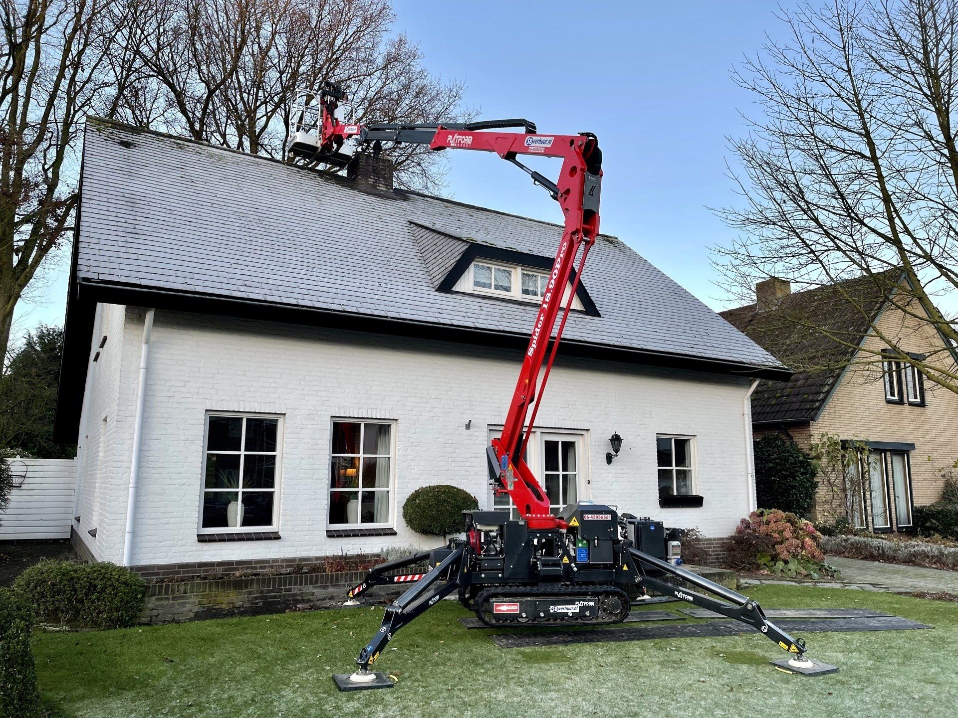 Een rode spinvormige hoogwerker staat op een gazon en strekt zijn arm uit om schoorsteen aan het dak van een wit huis uit te voeren.
PEVAHO Helmond
