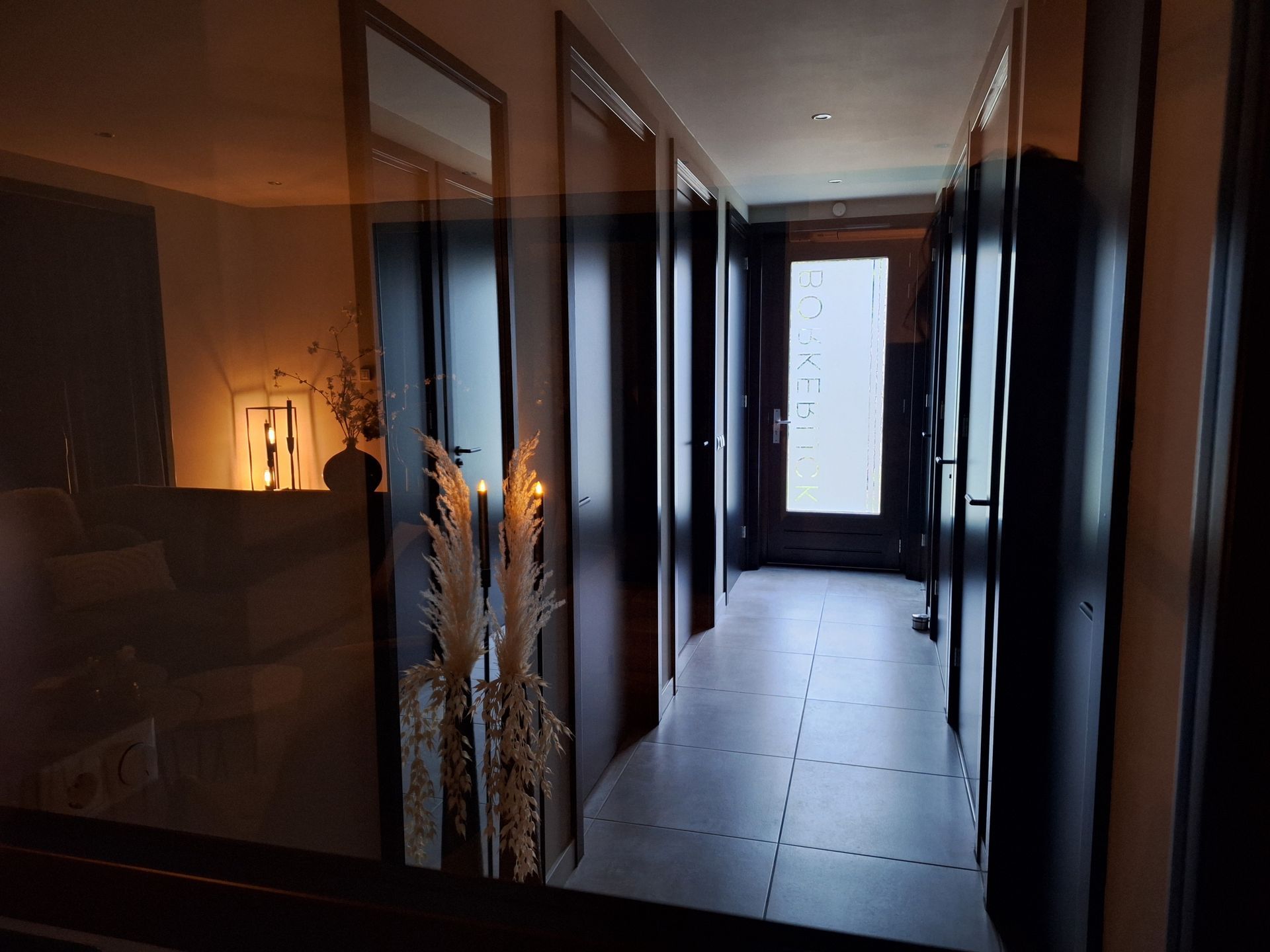 Gang met donkere deuren en een licht raam aan het einde, de weerspiegeling van een woonkamer in een spiegel.