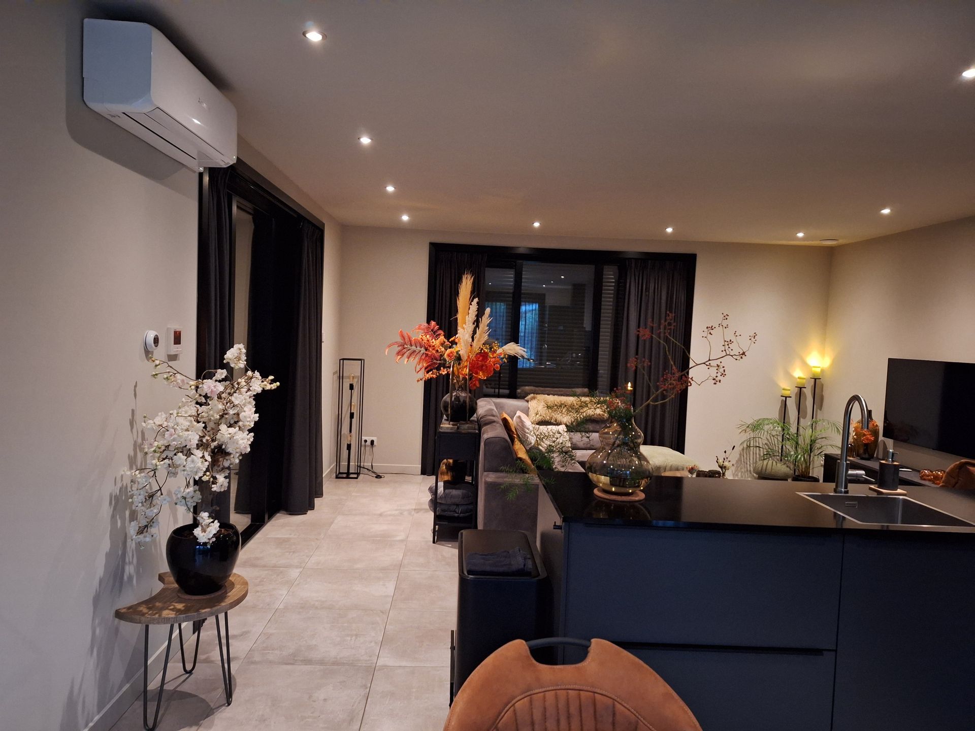 Moderne keuken met kookeiland, zwarte kasten en grote ramen. Witte muren en airconditioning. Bloemen sieren de ruimte.