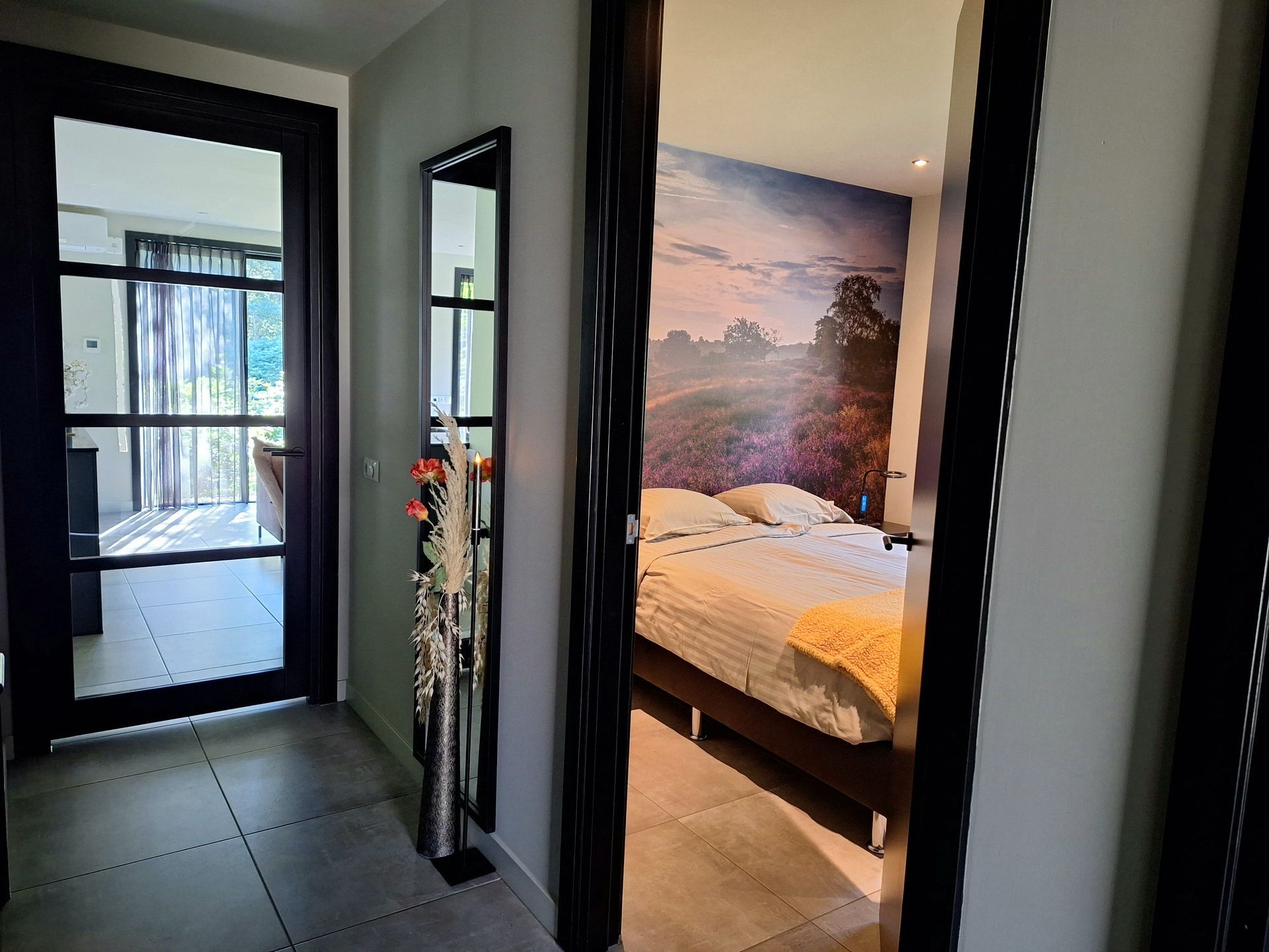 Hal met deuren naar een woonkamer en slaapkamer; een spiegel en een decoratieve vaas zijn zichtbaar.