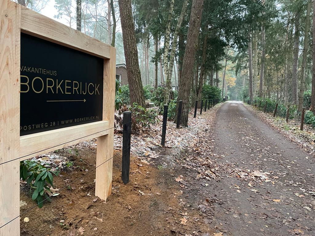 Bordje naar Borkerlock met pijl, onverharde weg omzoomd met bomen.