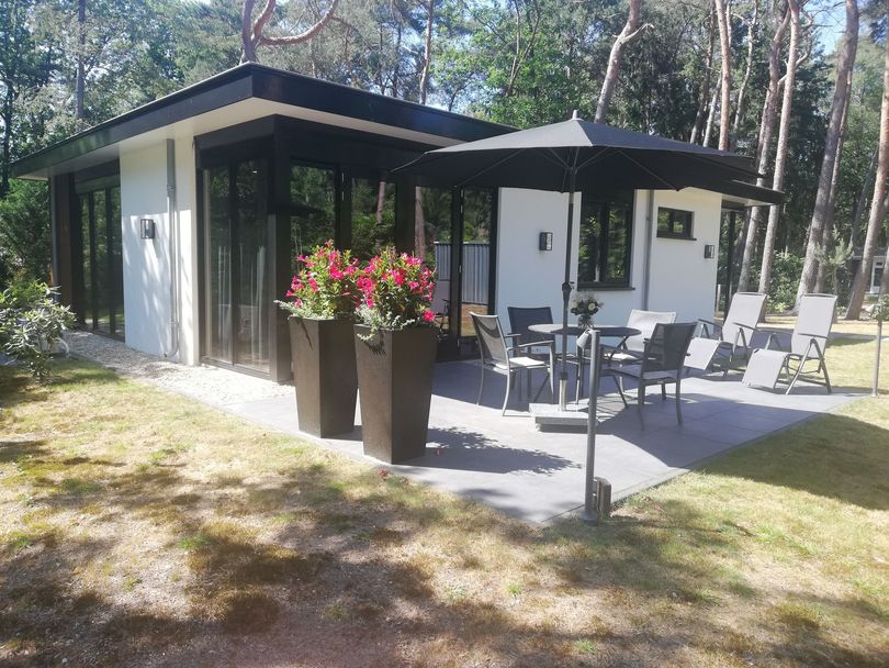 Modern wit huis met zwarte accenten en een terras met zitgelegenheid onder een zwarte parasol.