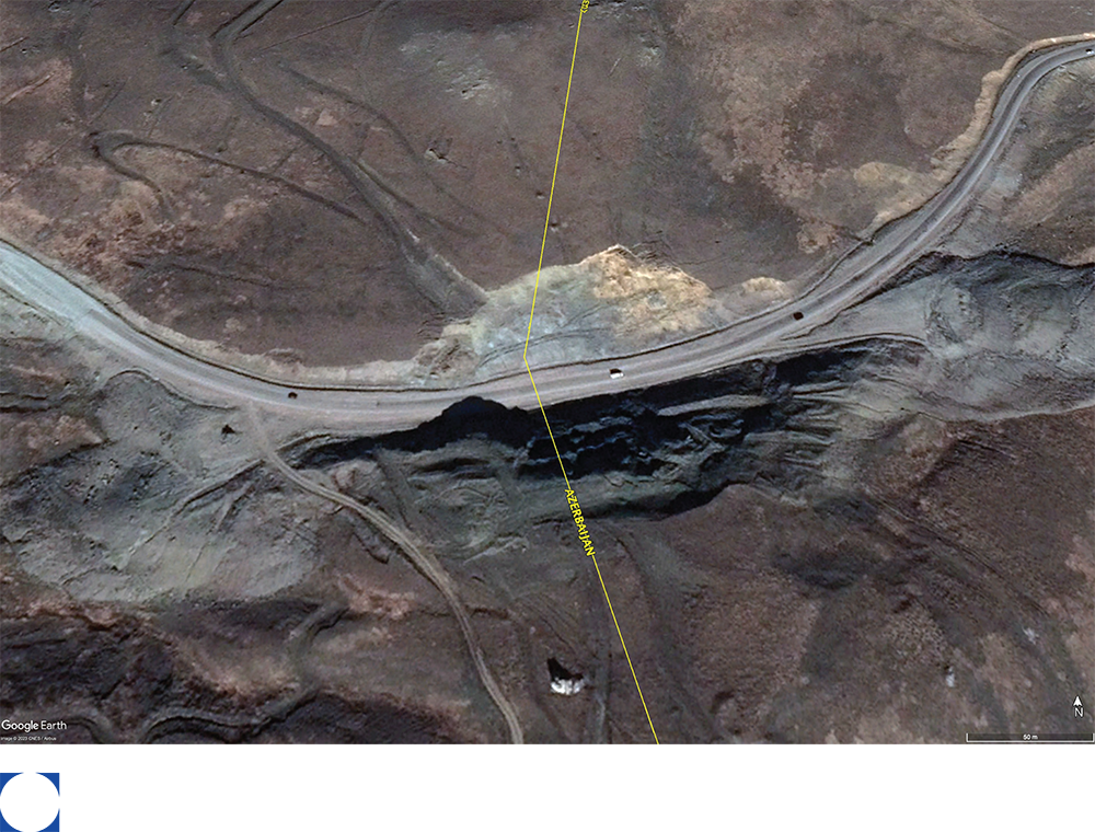 Overhead view of a mountain road winding over a bridge, surrounded by dark, rocky terrain. View of the Lachin corridor