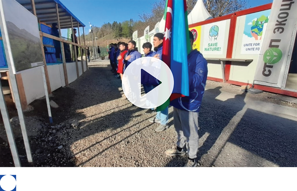 People standing outside a building holding flags in a park-like setting, shown in a ZPO press-release image.