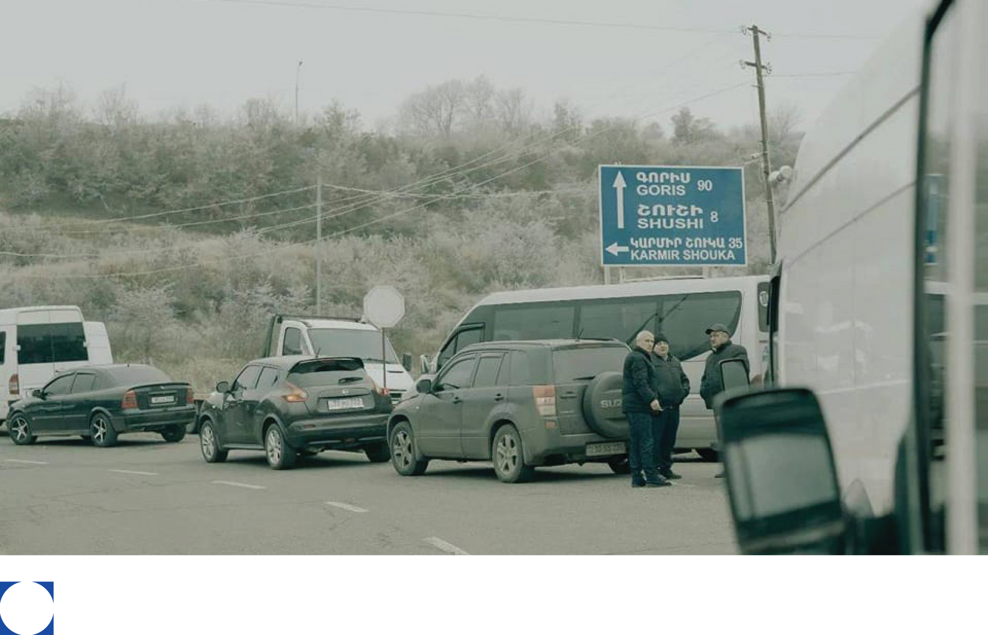 Cars and a bus stopped on a road, blue directional sign, two people in uniforms talking.