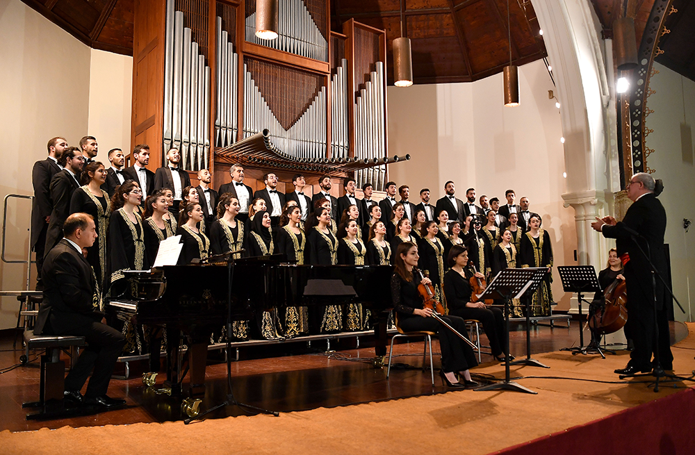 Conductor Barkev Taslakian & orchestra performing in a church with a large pipe organ. Armen Ketchek on the piano on the left