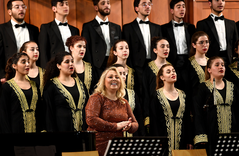 Maria Mattar in the foreground wearing a dress at the Giving Voice to Music concert at AUB Hall, with Al Fayha National choir
