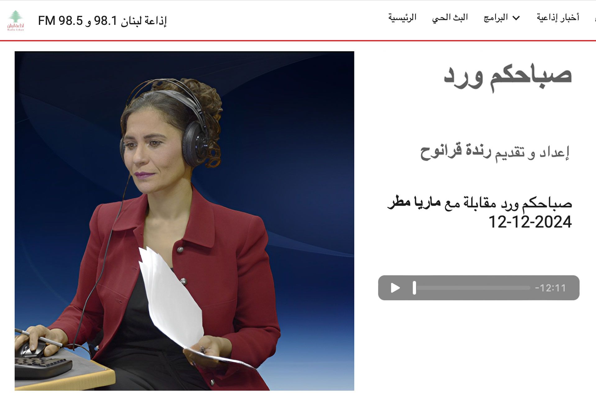 Woman in red blazer wearing a headset, presenting a broadcast with Arabic text.