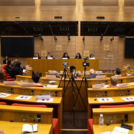 A Yazidi Genocide conference at the Palace of Luxembourg. People seated behind a long wooden table; audience in foreground.