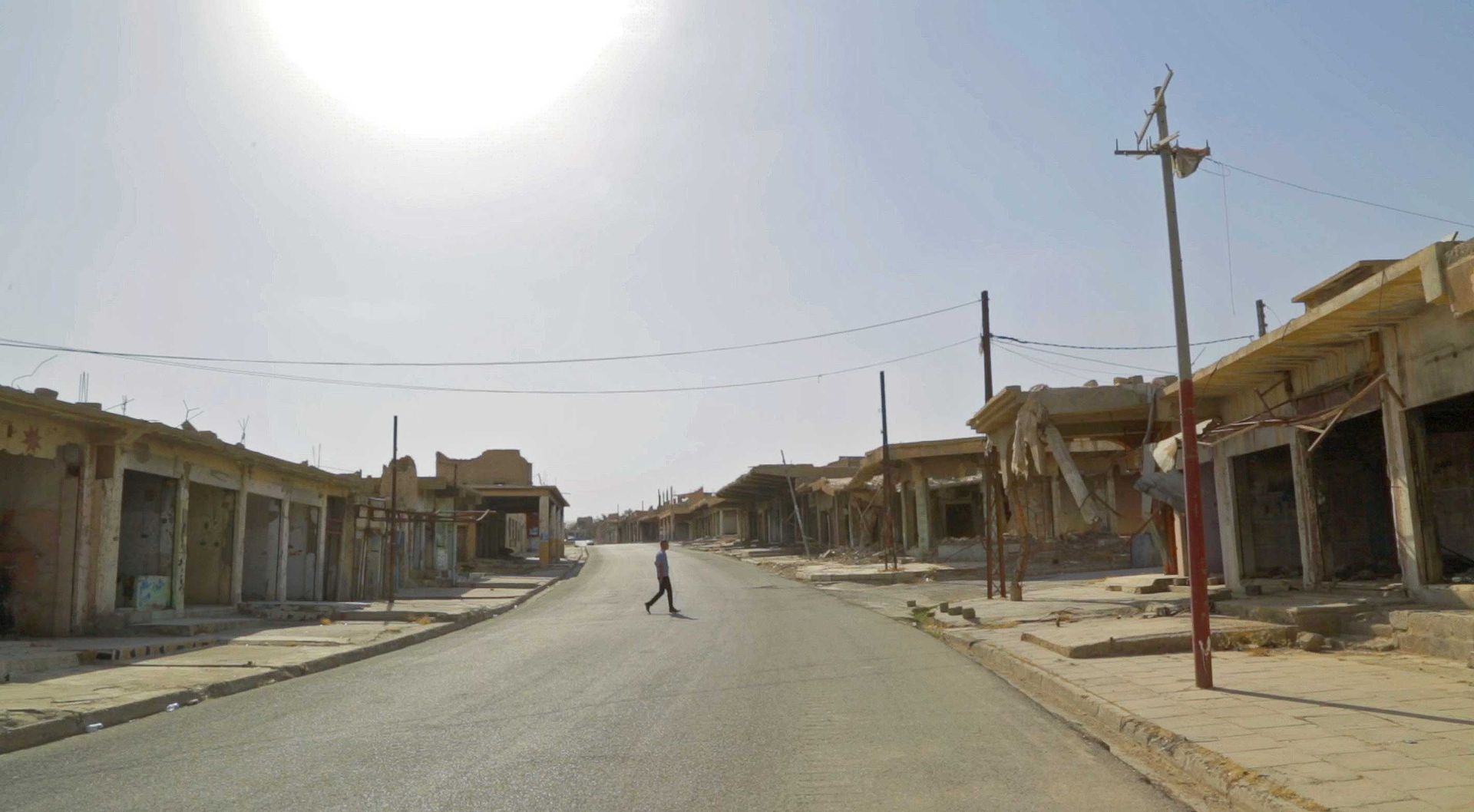 A person crosses a road lined with damaged buildings in Sinjar.Street in a war-torn area road in front of destroyed buildings
