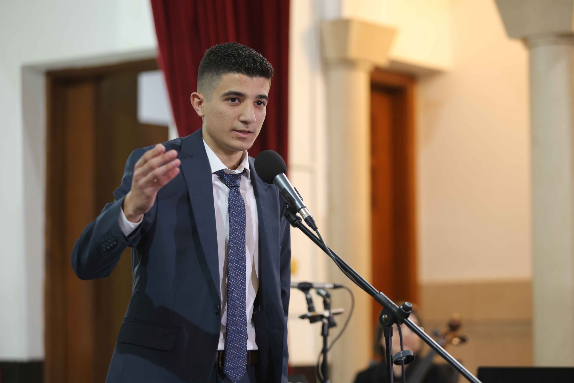 Iwan at the Giving Voice to Hope concert at AUB Hall wearing a tux and performing in front of a microphone.