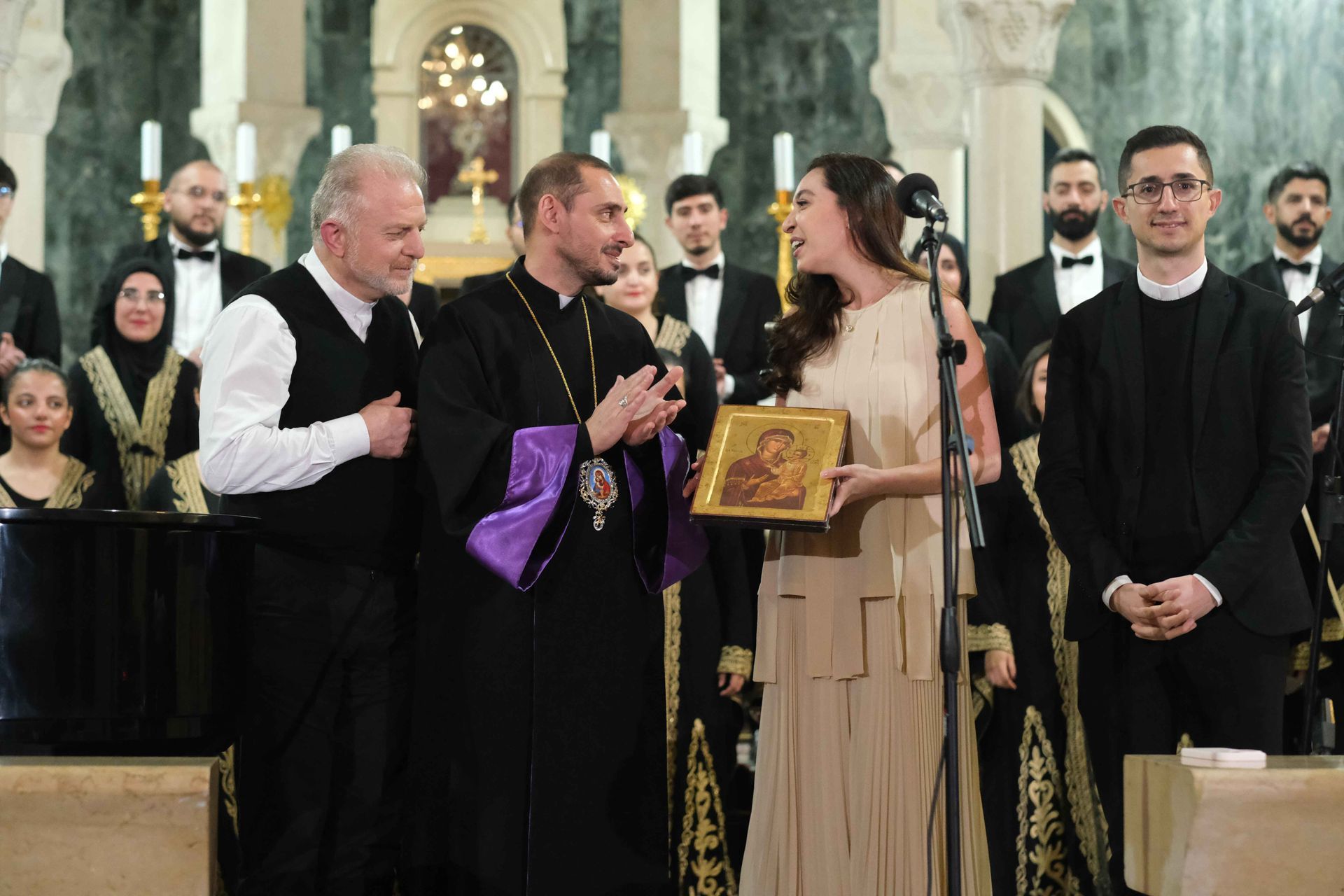 Lynn Zovighian in a beige dress receiving a religious icon from church members at Giving Voice to Hope concert at AUB Hall