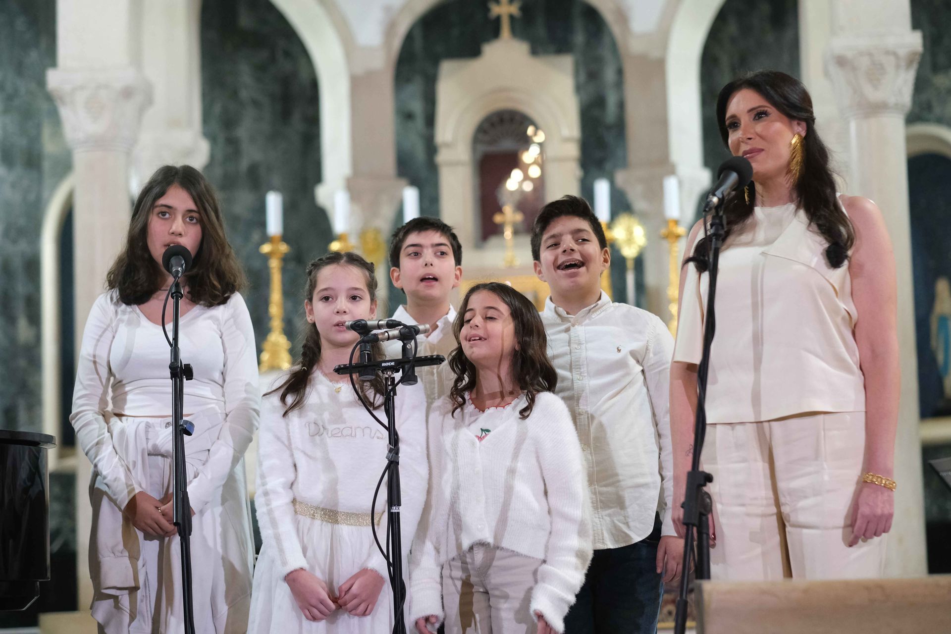 A group of children in white and a female signer performing at the Giving Voice to Hope concert at AUB Hall.