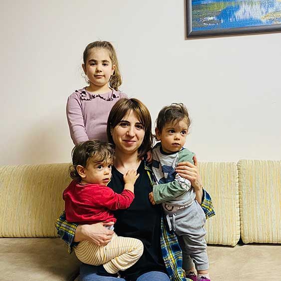 Image from “Mothers Blockaded” report showing a woman seated on a couch with three children hugging her.
