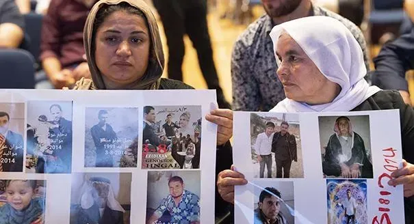 Diwan article; Two women wearing veils, holding photos, at an event titled