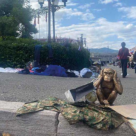 Press-release image showing a monkey statue covering its ears while sitting near clothes and a box on a sidewalk.