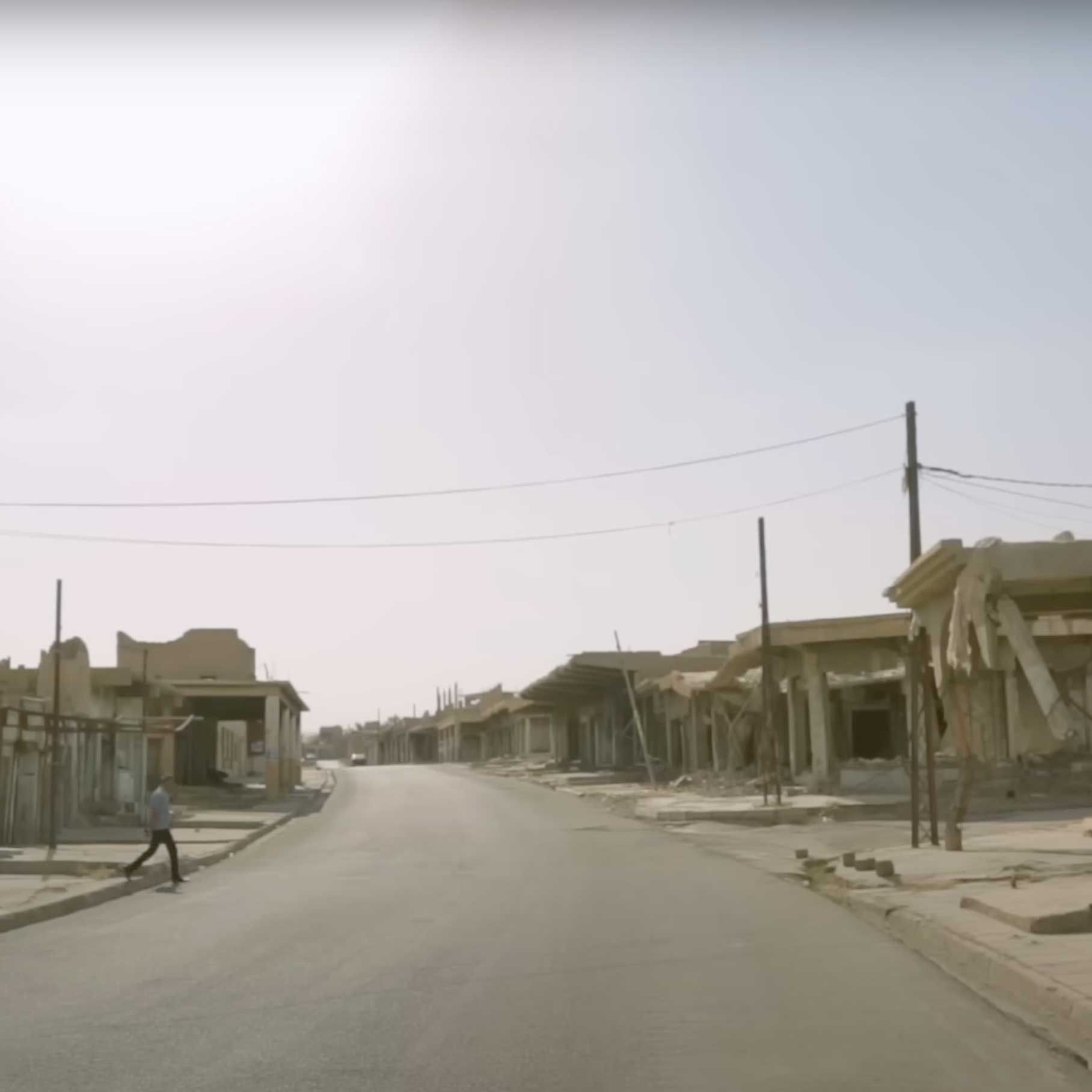 A person crosses a road lined with damaged buildings in Sinjar.Street in a war-torn area road in front of destroyed buildings